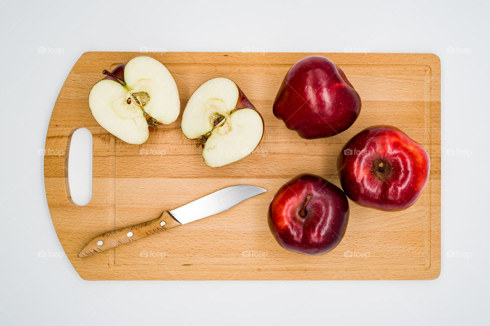 On a white background lies a wooden cutting board on which are red apples and a knife