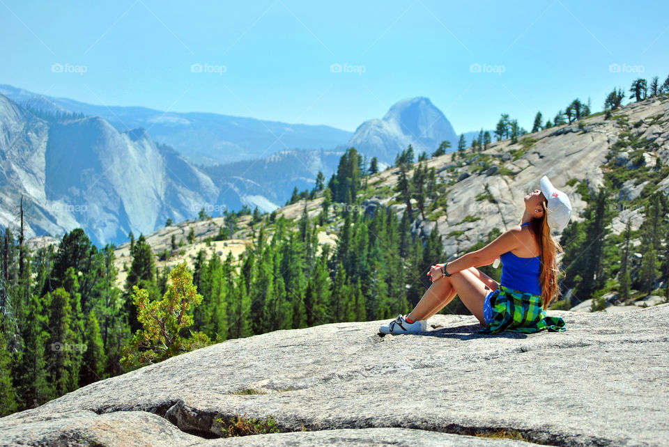 Woman relaxing, sitting, breathing fresh air after a long hike, on top of a rocky mountain, beautiful view