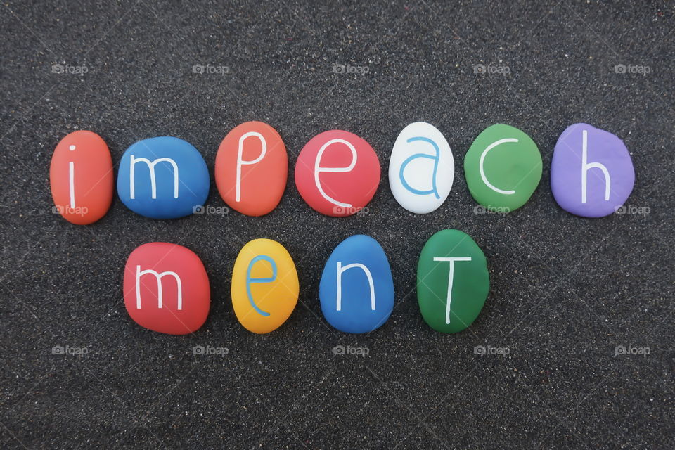 Impeachment word composed with multi colored painted stones over black volcanic sand