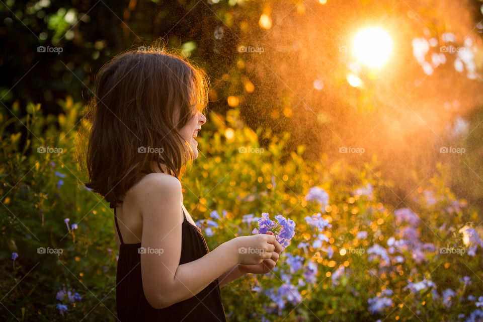 Smiling and having fun picking spring flowers at sunset. Image of girl laughing - outdoor image.