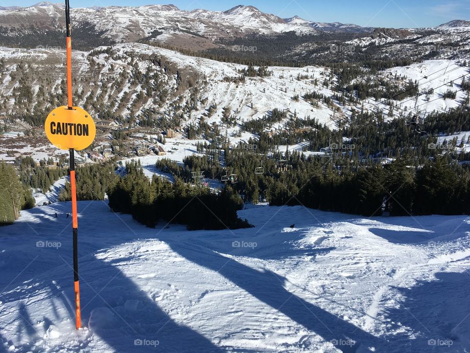 The top of a snow covered ski slope with a yellow caution sign