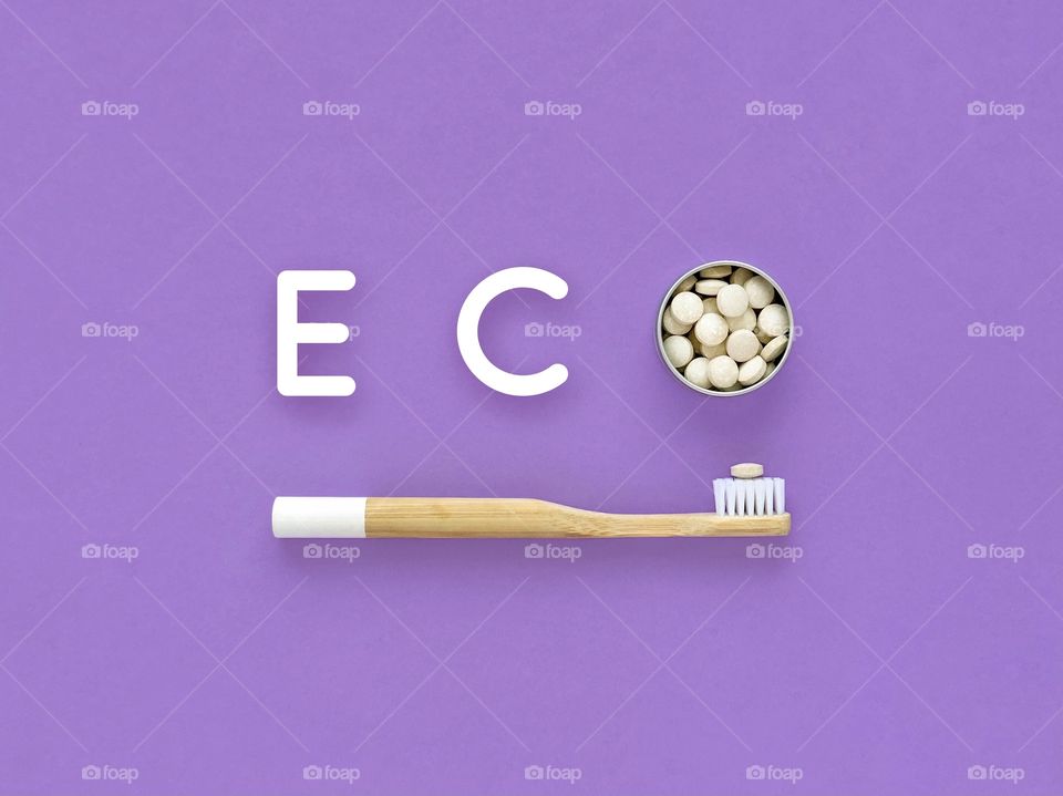 Bamboo toothbrush and toothpaste in tablets. Word Eco on a violet background. Plastic free.