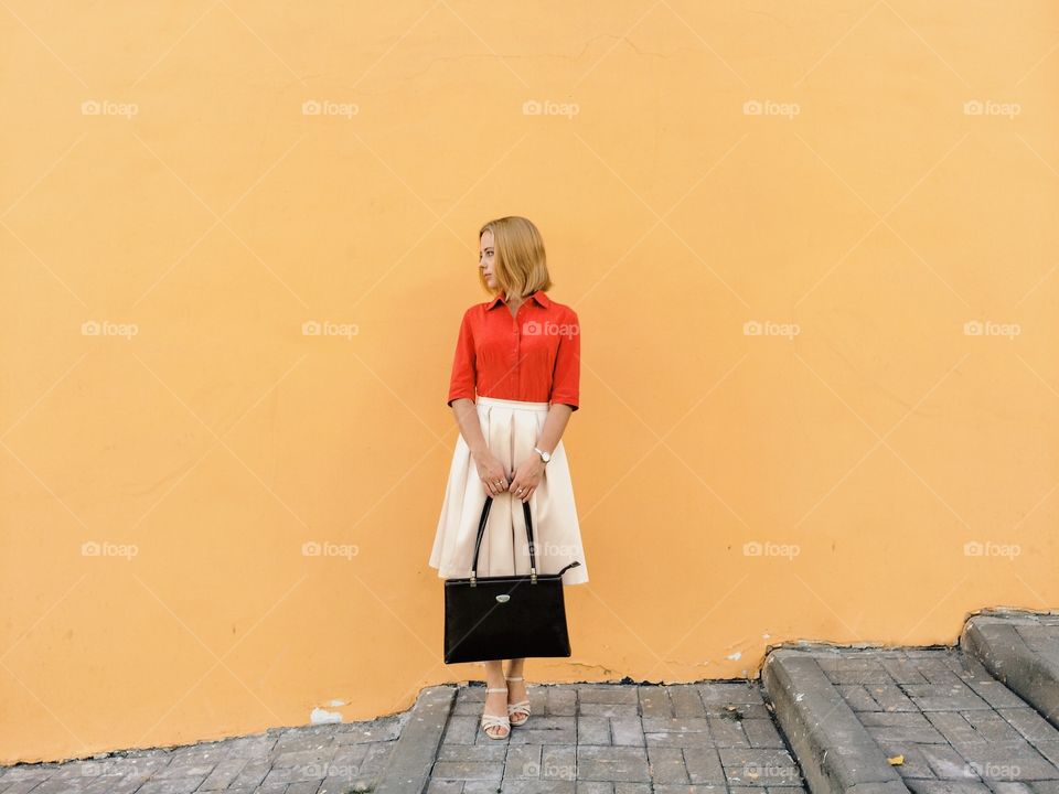 Girl standing against yellow wall with holding hand bag