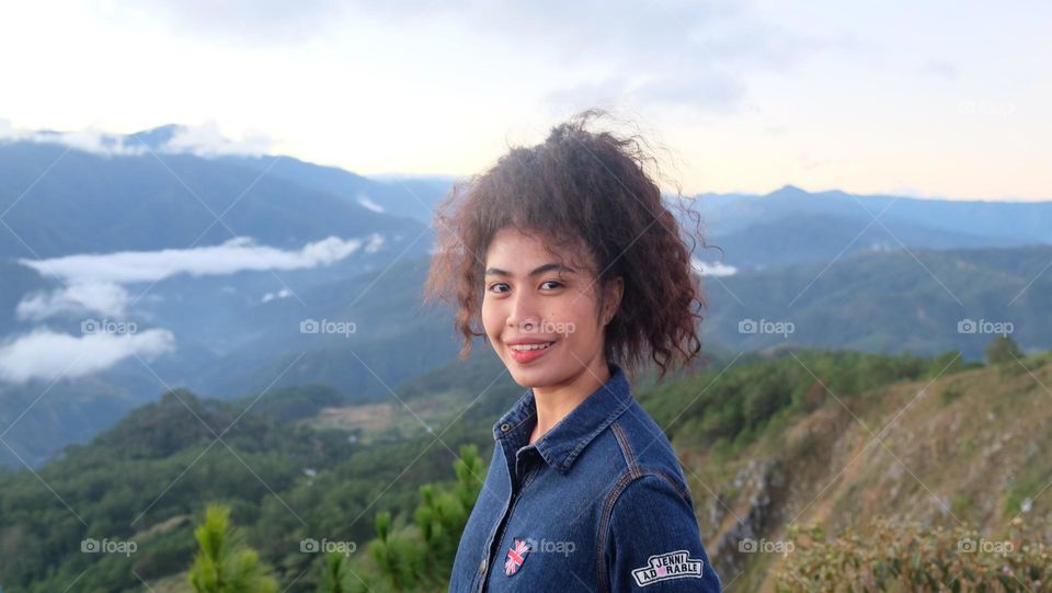 Curly haired Filipina standing atop a mountain