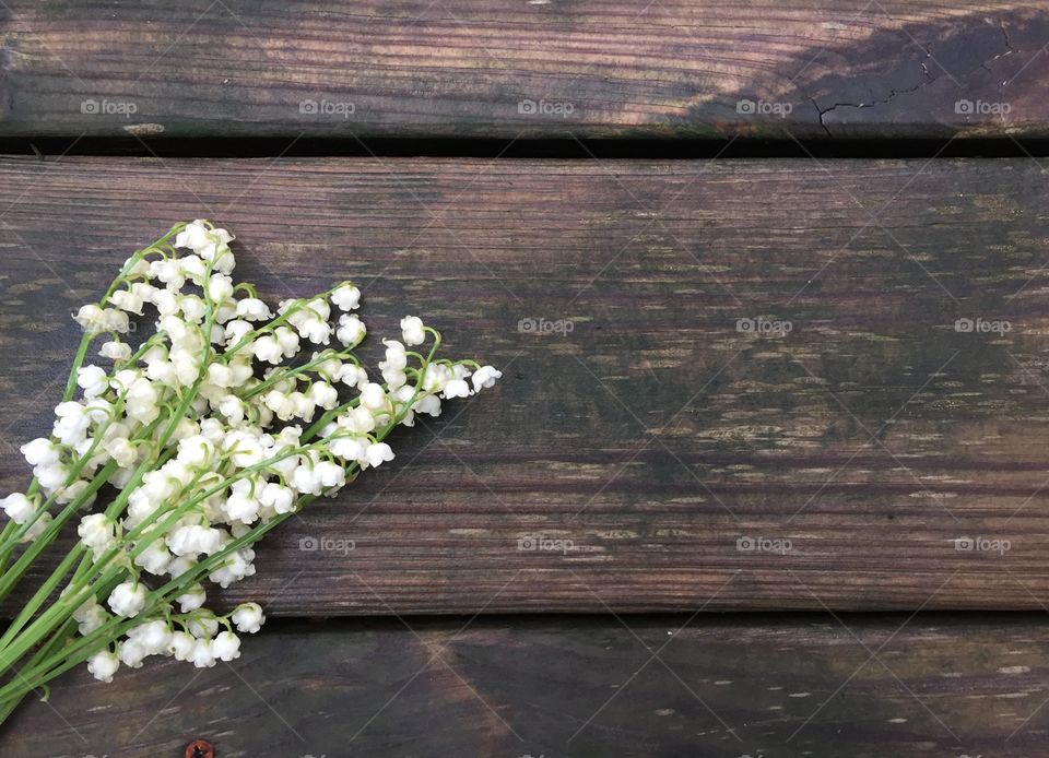 Lily of the valley flat lay on a dark, rustic, wooden surface (landscape)