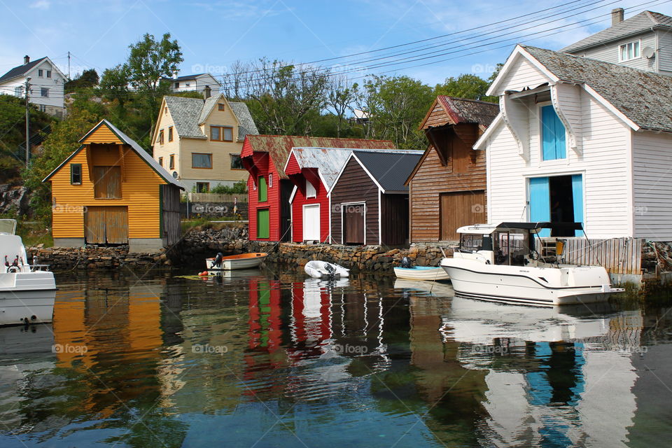 Bright view of dock by red, white and orange houses with clear reflecting water in sunlight in Glesvær on Sotra, Norway