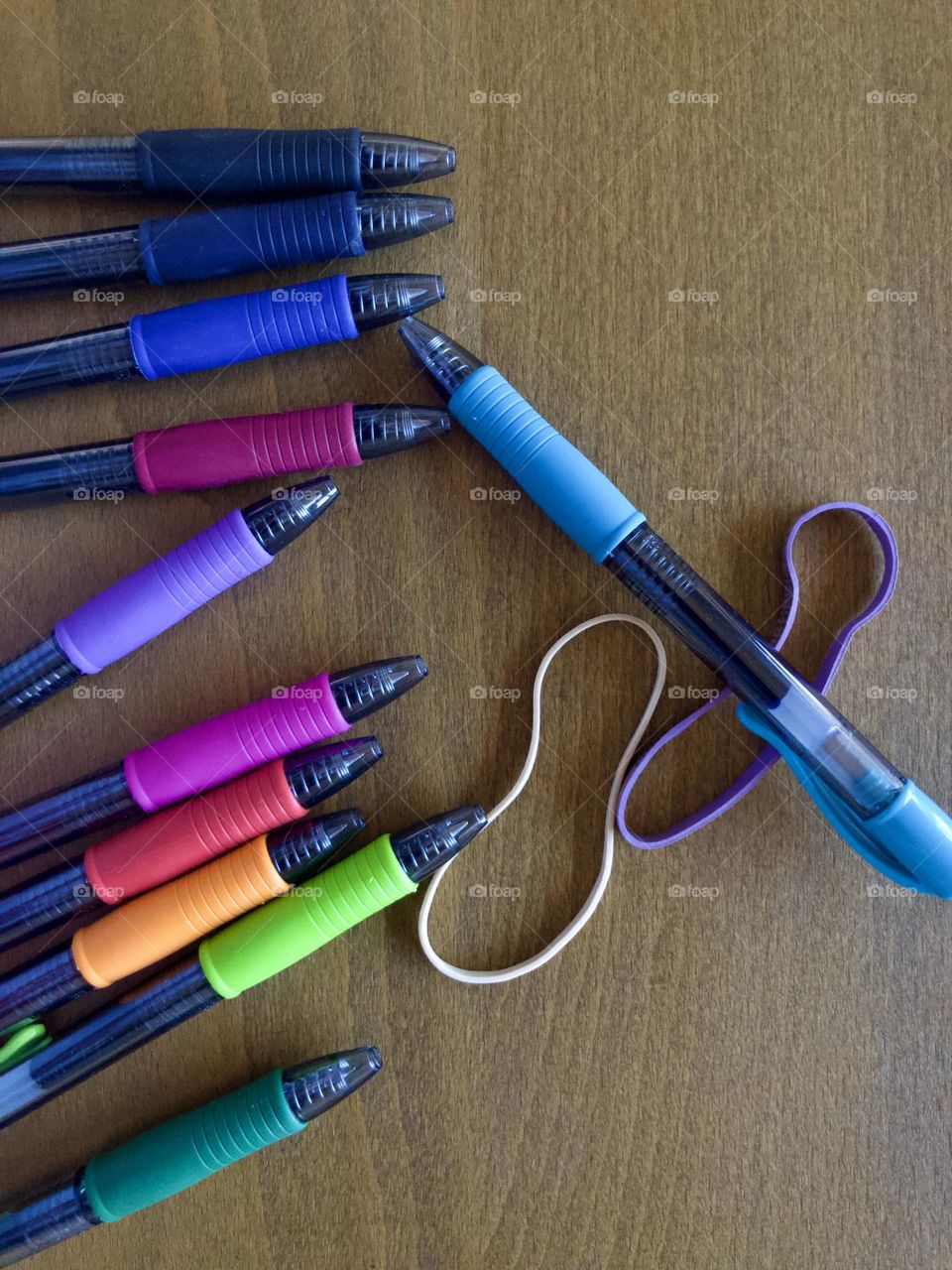 Overhead closeup of colorful drawing pens and rubber bands on desktop. The tools create their own still life.