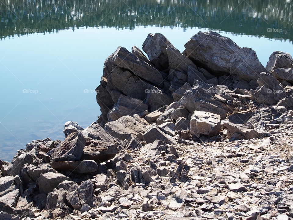 Jagged rocks and boulders along the shoreline of Ochoco Lake in Central Oregon on a sunny spring day.