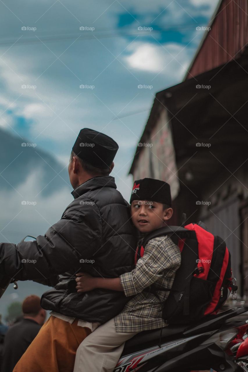 A cute boy looks to the side while on a motorcycle driven by his father