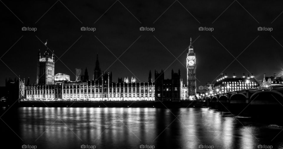 Black and white photograph of the Houses of Parliament London, UK. Shot at nighttime with the river Thames in the foreground and Westminster bridge to the right.