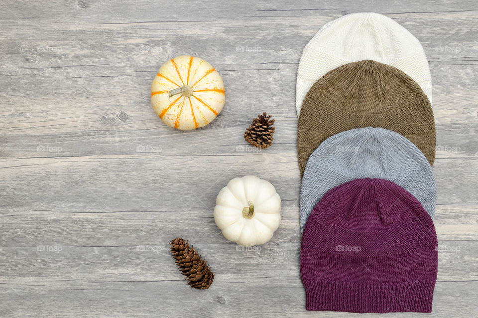 Row of knit beanie hats next to pumpkins and pinecones