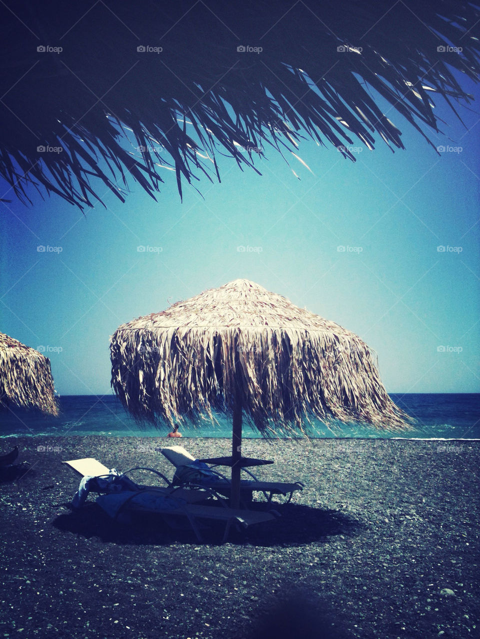 Lounge chairs under a straw umbrella on the beaches if Santorini,