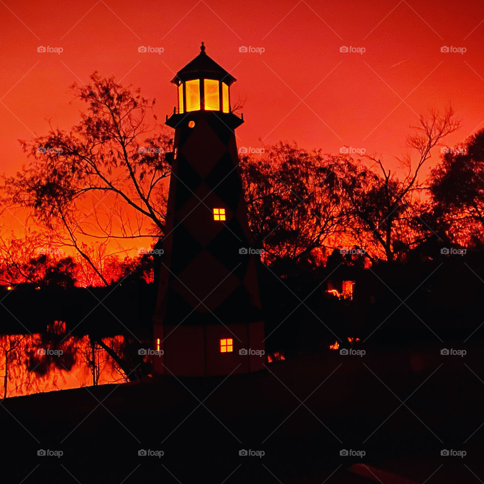 Evening sunset lighthouse firmed position. Colors of backlit spreading reflections on lakebed waters. 
