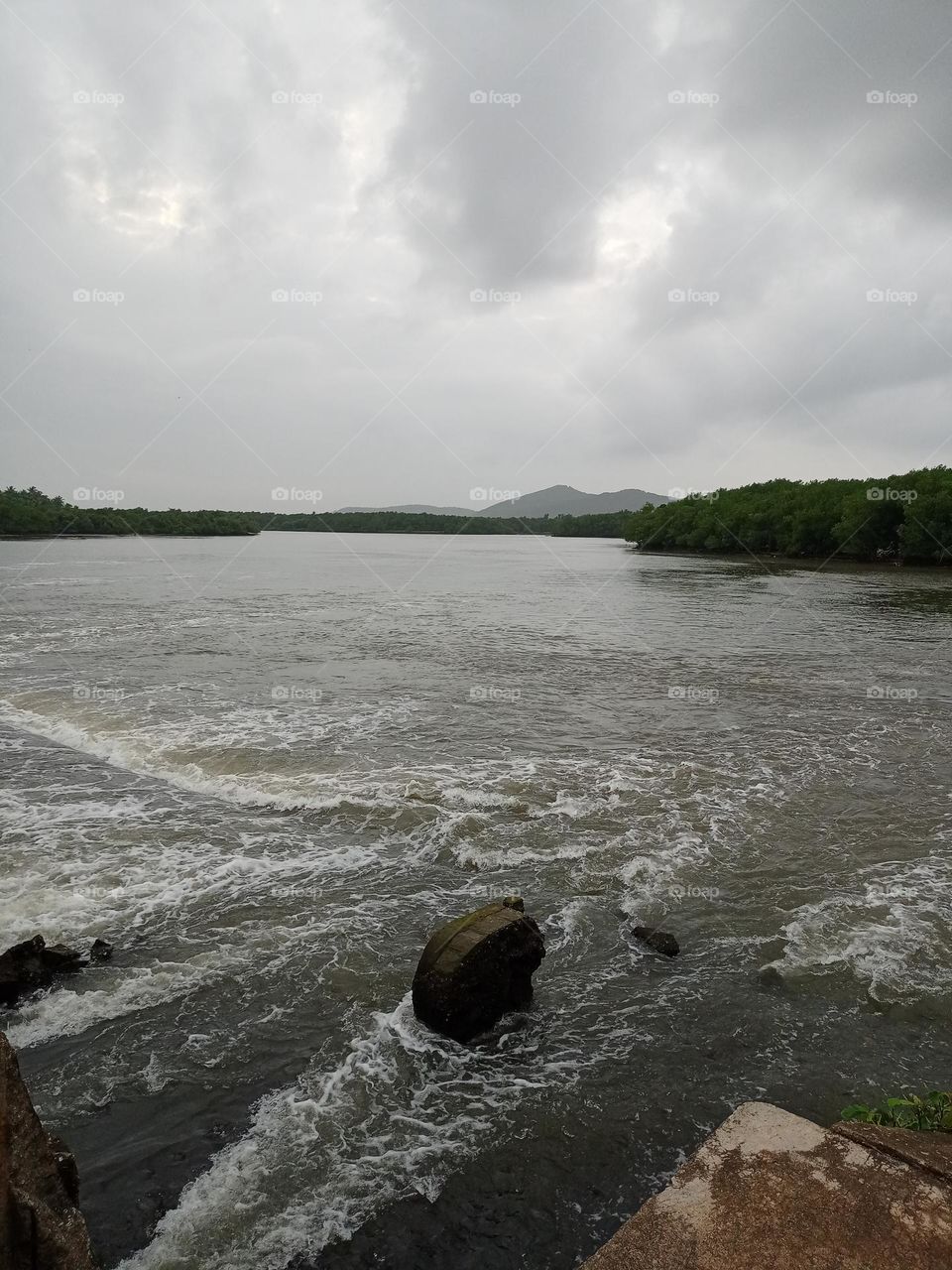 Big rock on the middle of river heavy water flowing with nice background of mountain cloud and sky