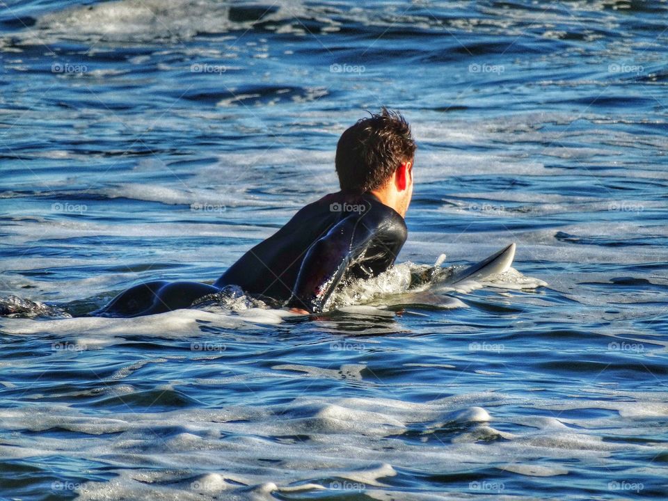 Surfer in wetsuit paddling into the waves in Pacifica, California