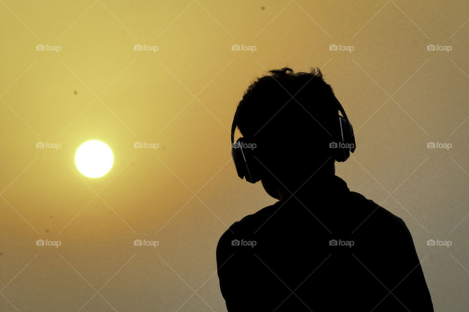 Silhouette of man man listening music with headphones on sunset sky background.