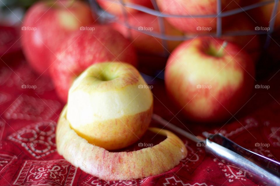 Fruits - Gala apples in a wire basket with a partially peeled apple and peeler on a red bandana-print tablecloth