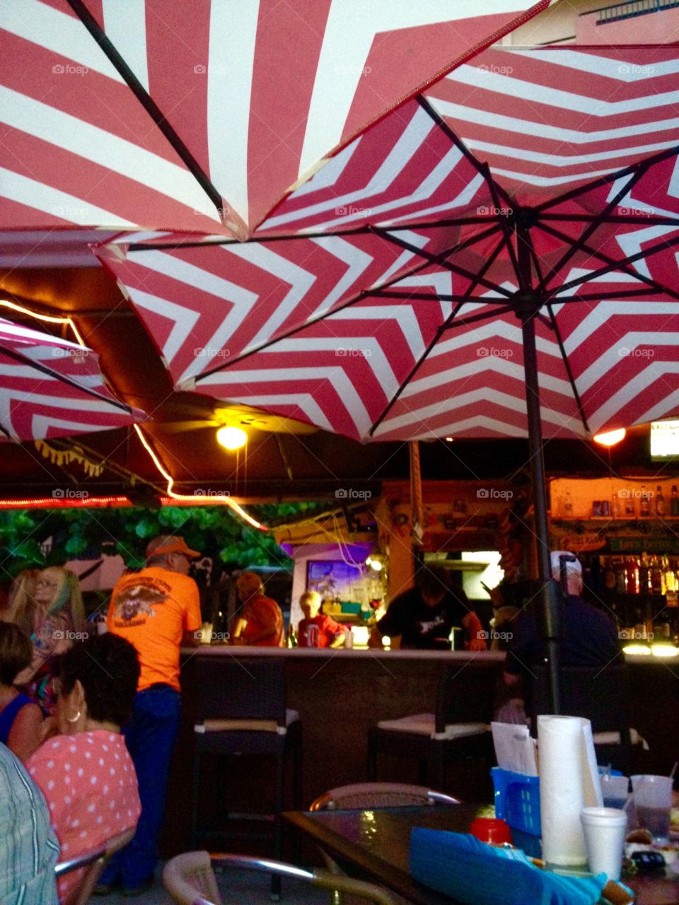 Outdoor bar and restaurant in summertime with tables covered by pretty red & white striped umbrellas.