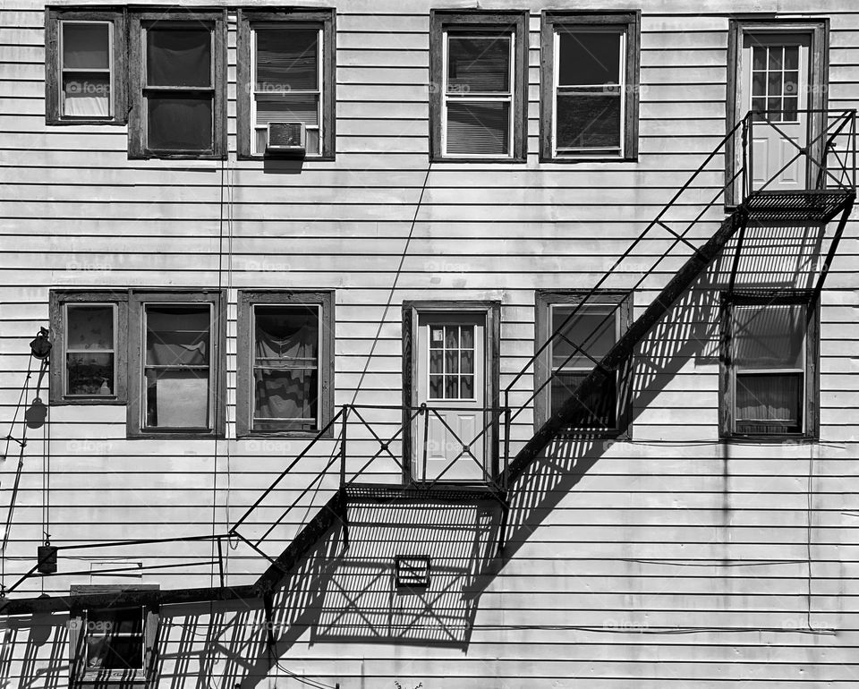 Fire escape and its shadow on the side of a wooden building 