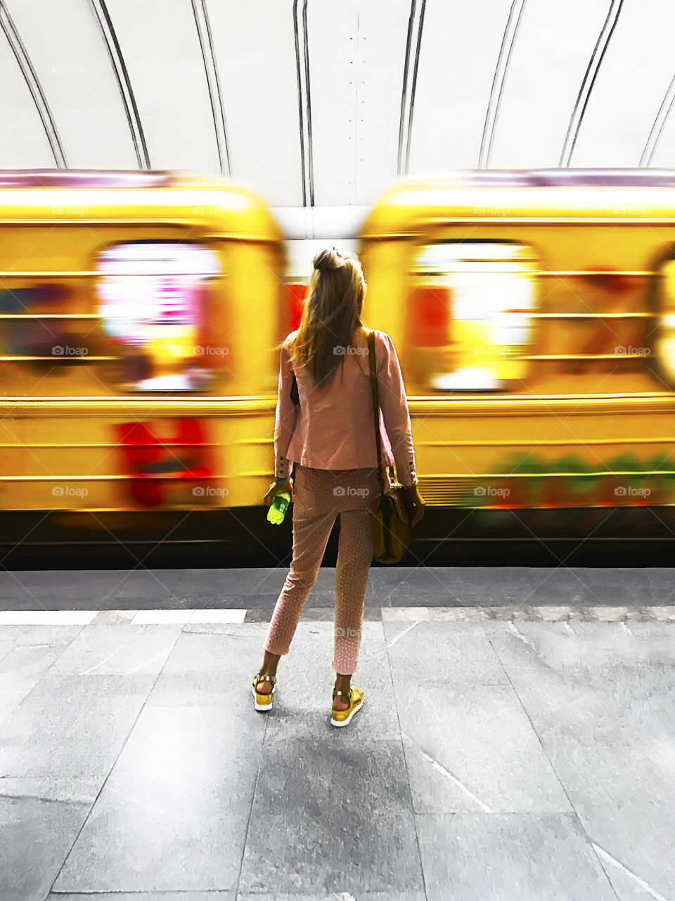 Young woman standing in front of a moving yellow train at city subway station 
