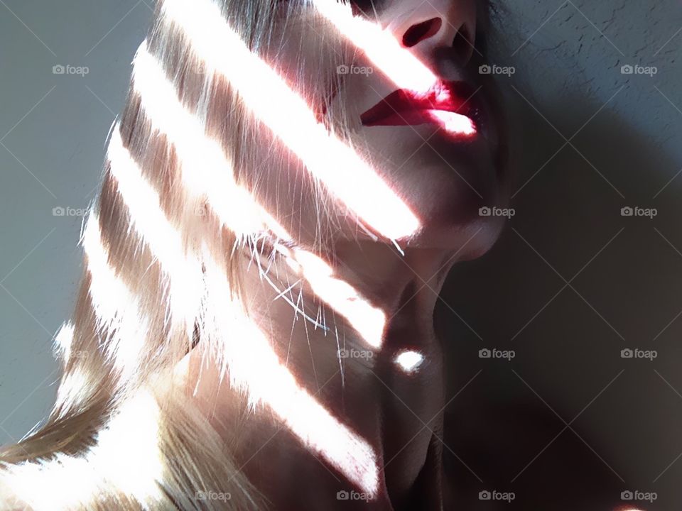 Golden light rays and shadows providing interesting streaks on a woman’s face and neck.