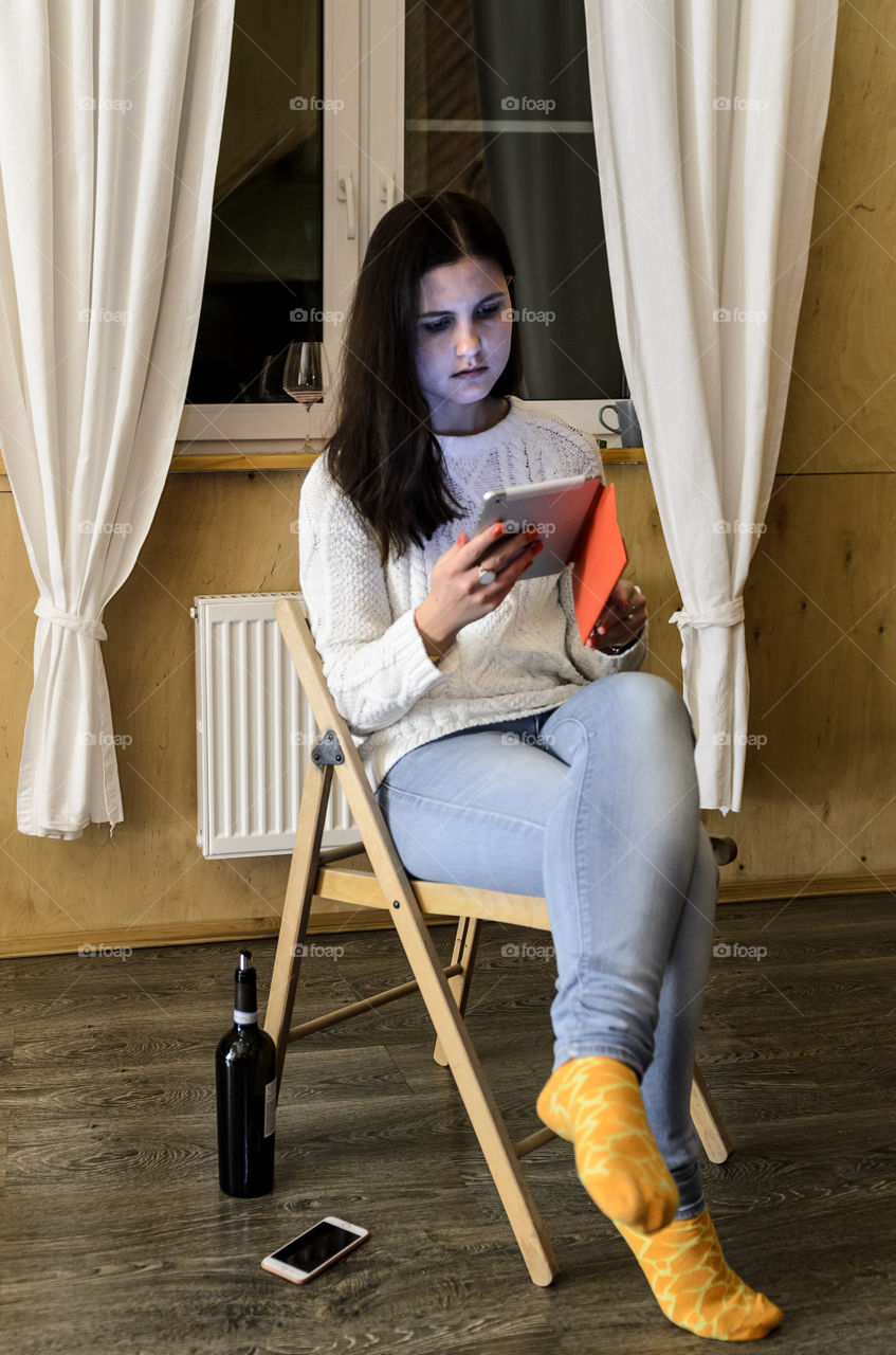 Girl reading from ipad and sitting on a chair at home