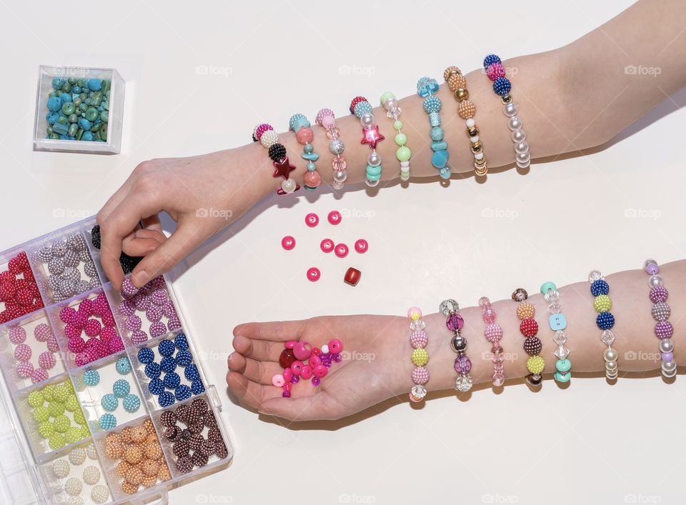 Girl reaches for more colourful beads to create her pretty bracelets that she displays on her arm - a creative hobby