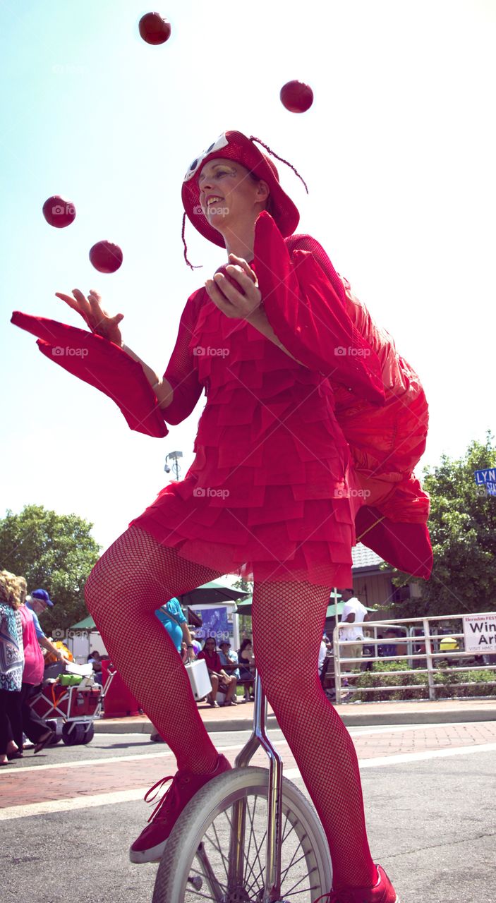 Please Don't Fall!. Woman wearing a crab costume, juggling and riding a unicycle. 