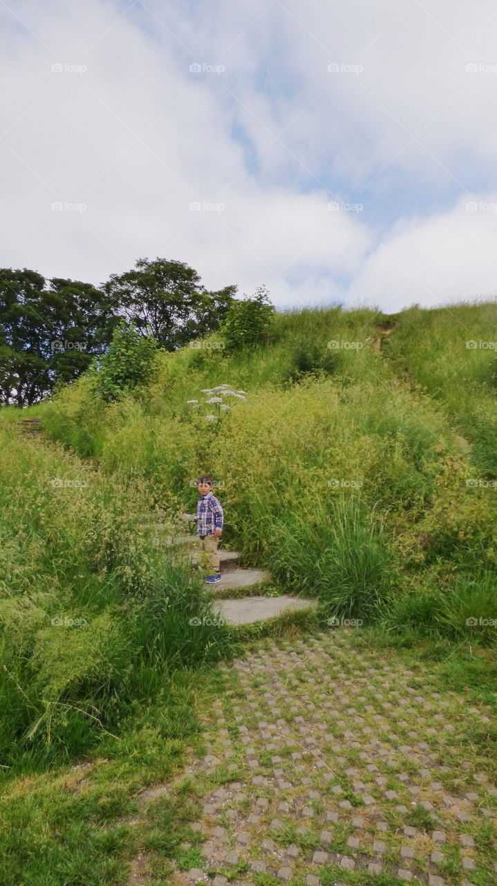 little boy is walking up the stairs covered in green grass outdoors in nature going up the hill