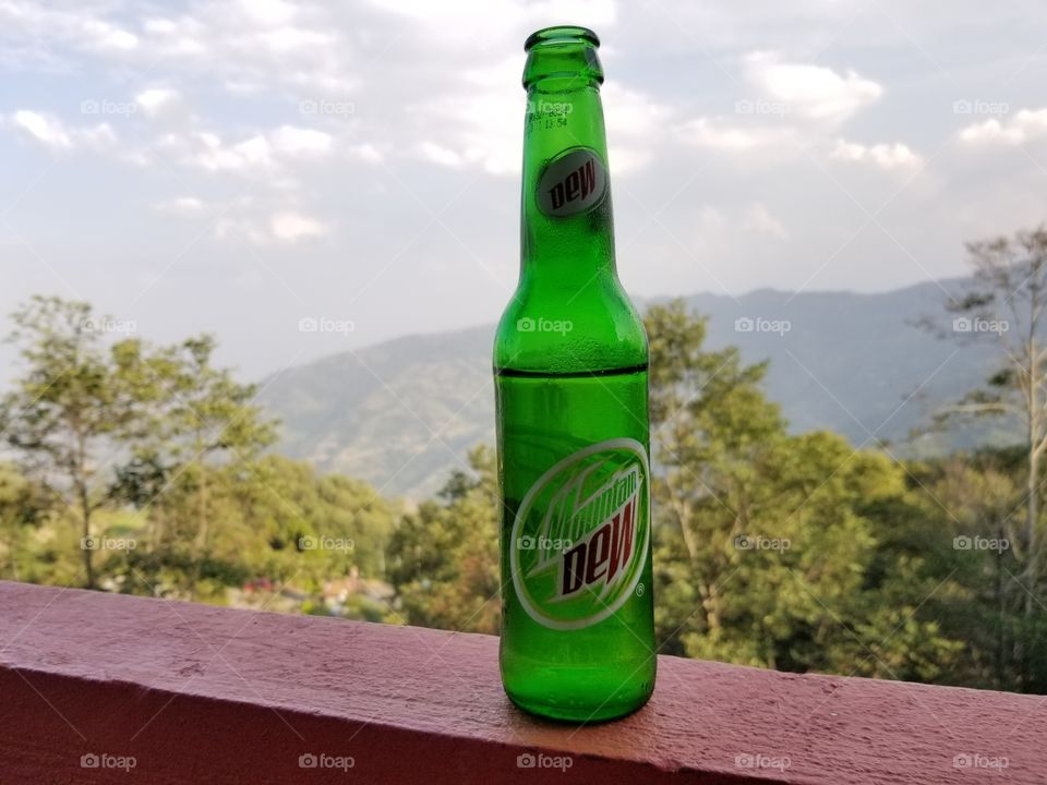 cold, refreshing glass bottle of Mountain Dew in taken in Nagarkot, Nepal. The mountains in the background are of the Himalayan foothills.