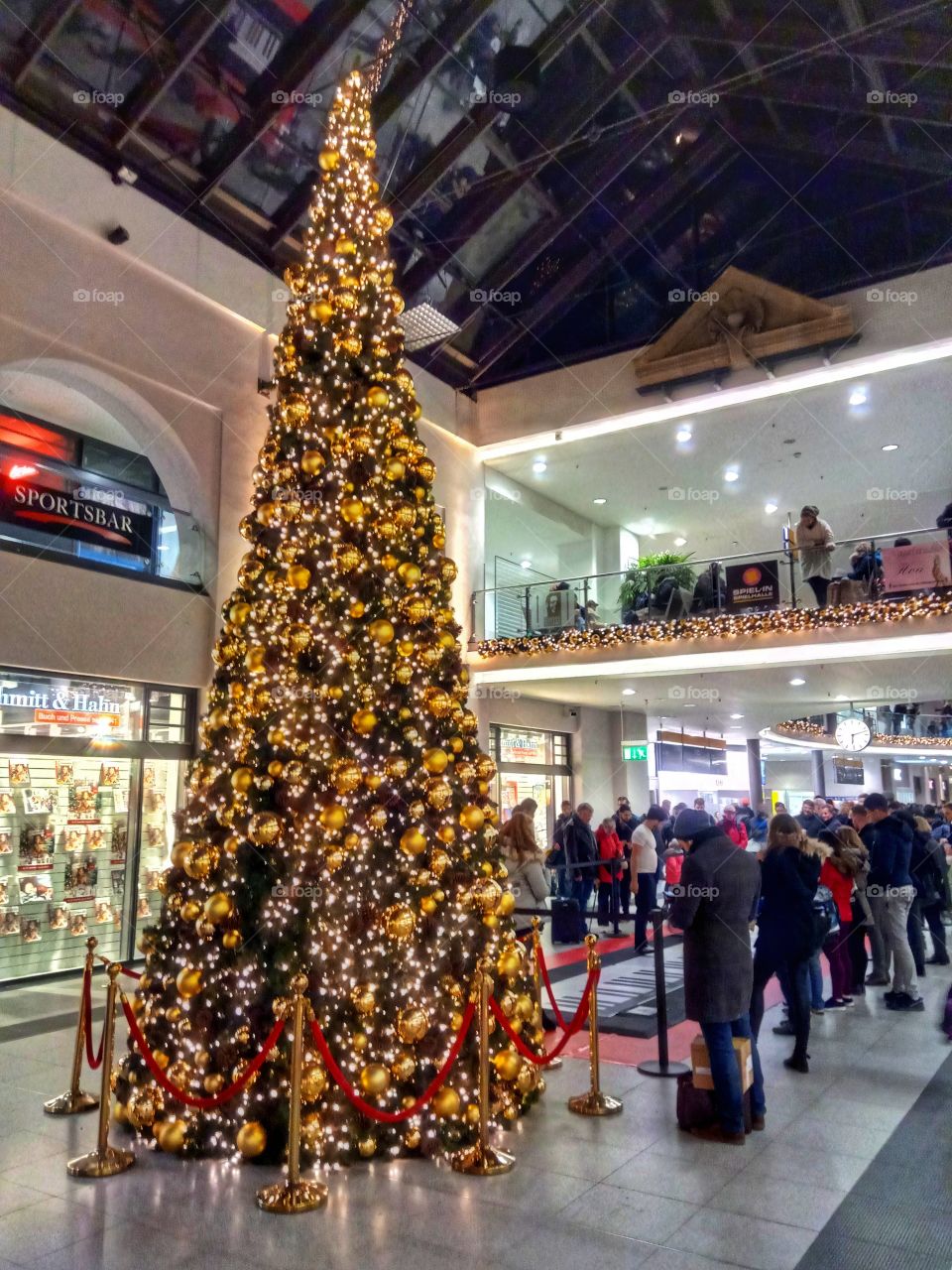 A big Christmas Tree with many decorations and a group of people standing around it