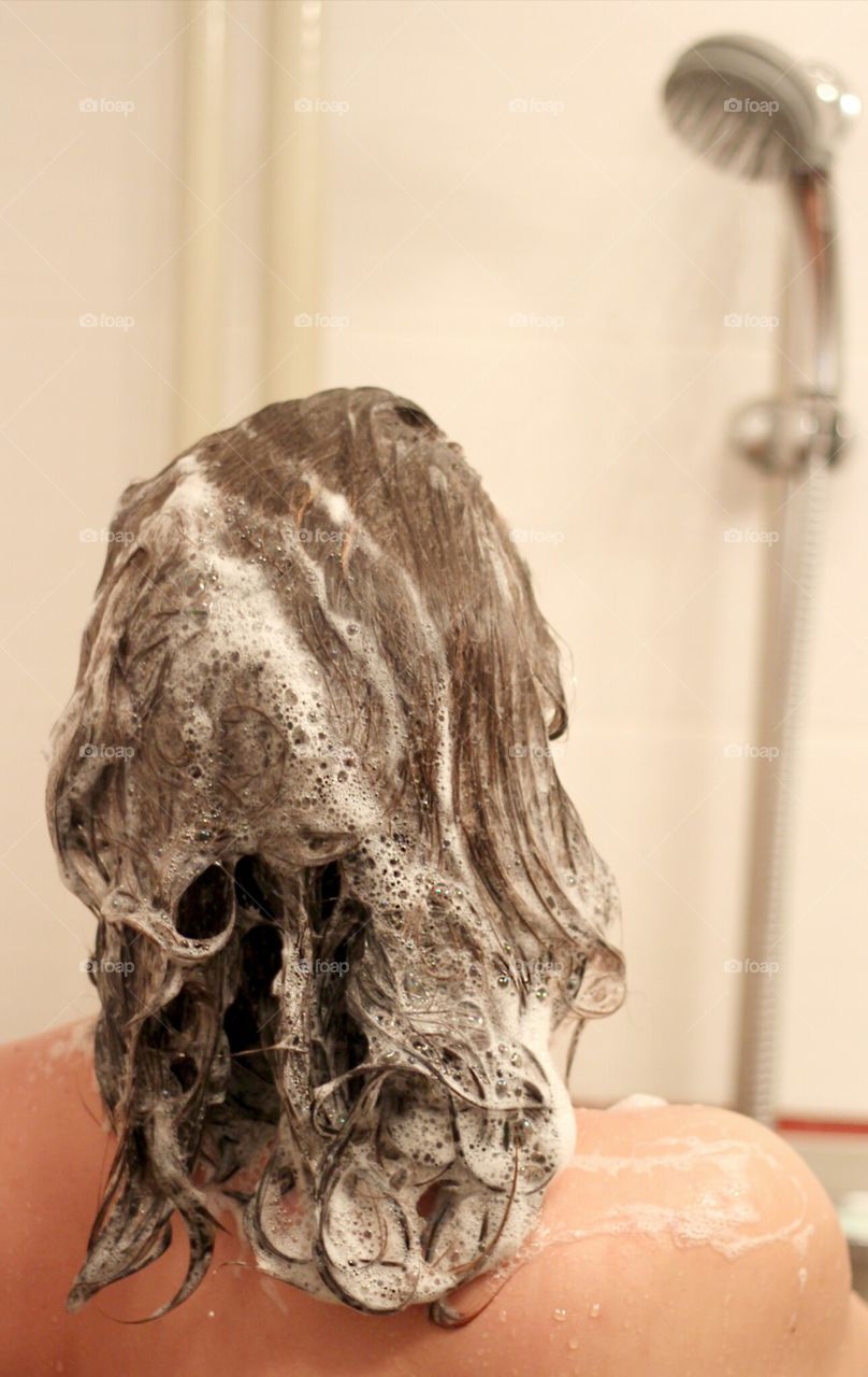 A woman taking shower, shampoo foam in her hair