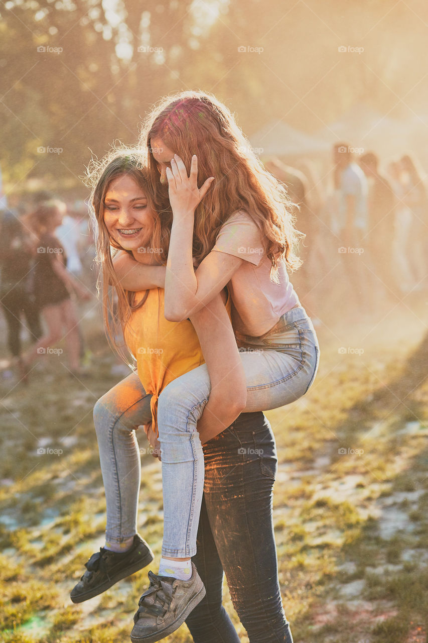 Portrait of happy smiling young girls with colorful paints on faces and clothes. Two friends spending time on holi color festival. Real people, authentic situations