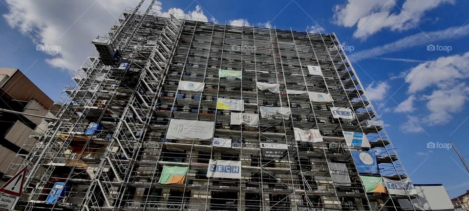 This modern high rise construction site with multi story scaffolding and various banners affixed to it is sort of an unusual sight, especially for “Munich”, “Bavaria”, Germany. 2022. Hypnotic Productions