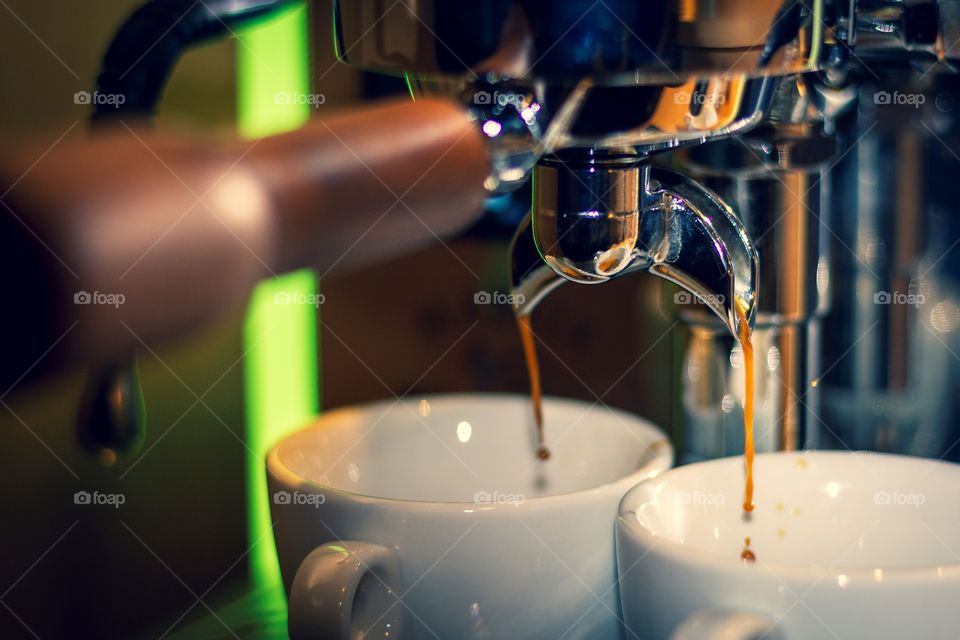 A portrait of the portafilter of a coffee machine. there is coffee pouring out of the two nozzles of the portafilter.