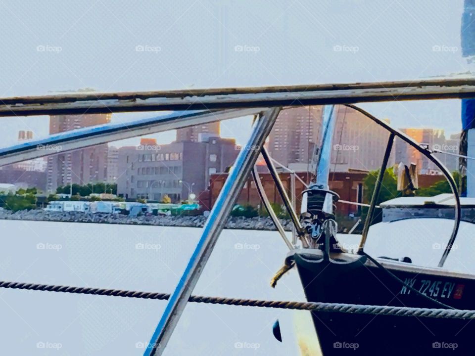 The aluminum railing of our sailboat, the „Salvation“ in the foreground, a neighboring boat, view of the water and of the Long Island City, Queens, NY skyline on the other side of the East River. 2018. Hypnotic Productions