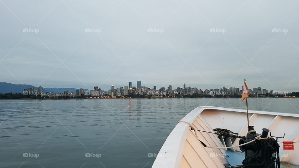 the bow of a boat approaching city skyline at dusk on calm ocean