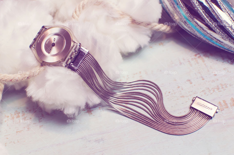 Vintage Swatch watch on rustic blue wood background with white fluffy pompon background elegant curves and fluid motion of a silver bracelet band