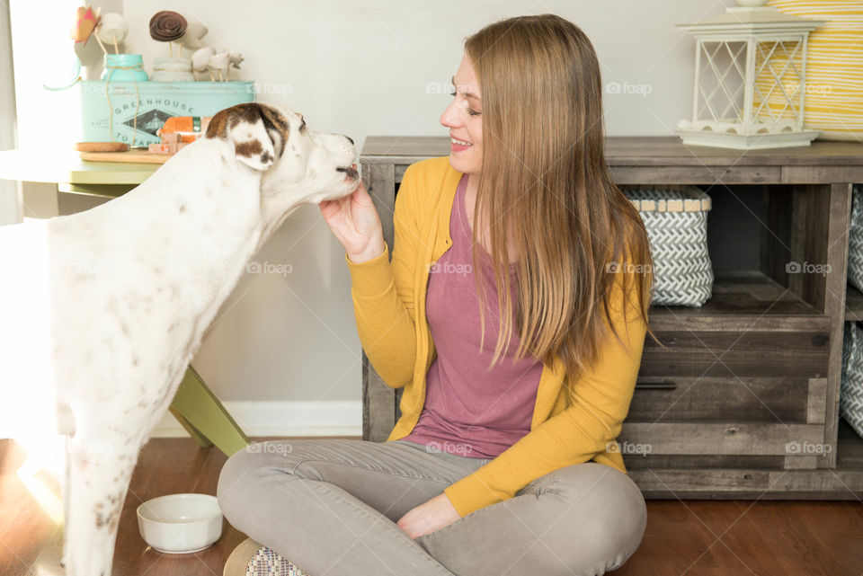 Young woman sitting on the floor and feeding her dog