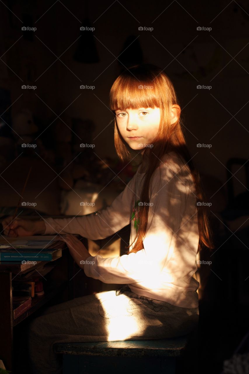 Little girl draws at a table in the setting sun