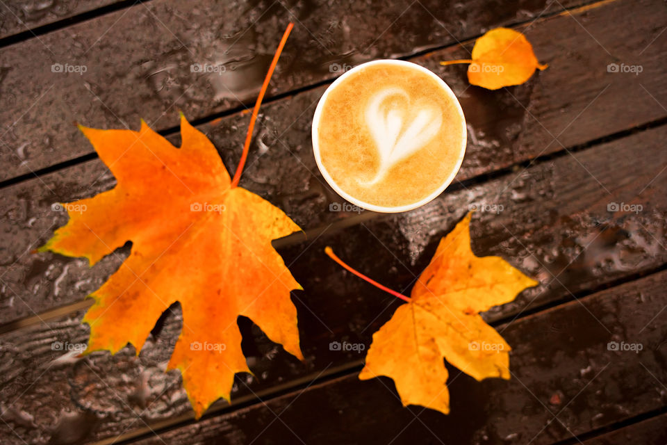 Latte cappucino art with bright vivid maple leaves on wooden wet table