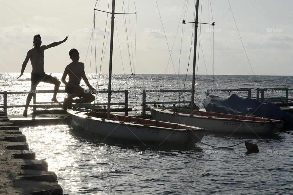 Father and son jumping to the water from the dock at sunset 