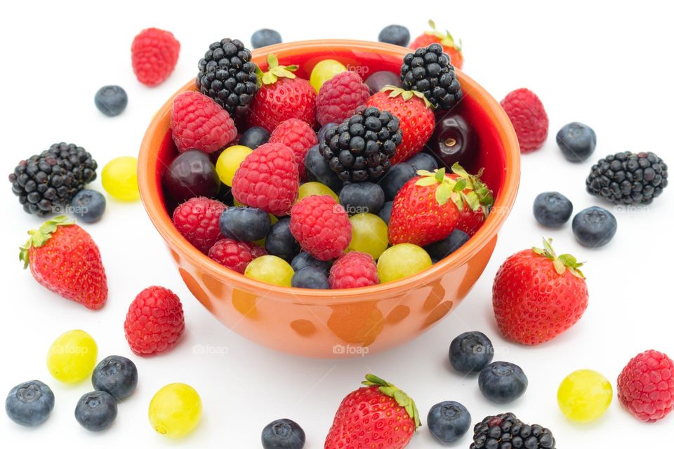 Ceramic bowl full of mixed forest fruits (blueberries, raspberries, blackberries and strawberries), cherries and grapes. White background full of mixed fruits