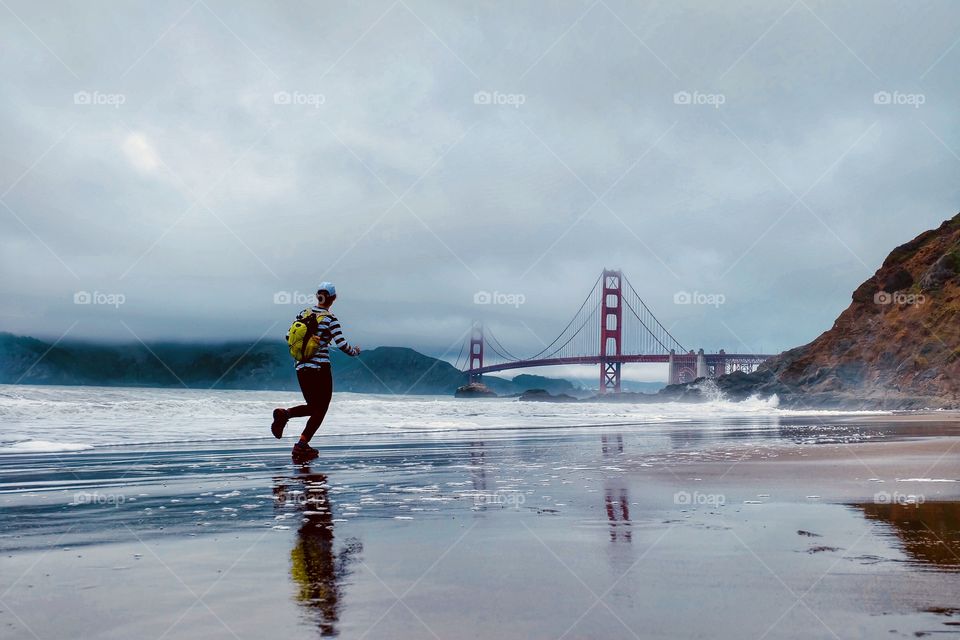 A lady runner running on Baker Beach in San Francisco towards the Golden Gate Bridge.
