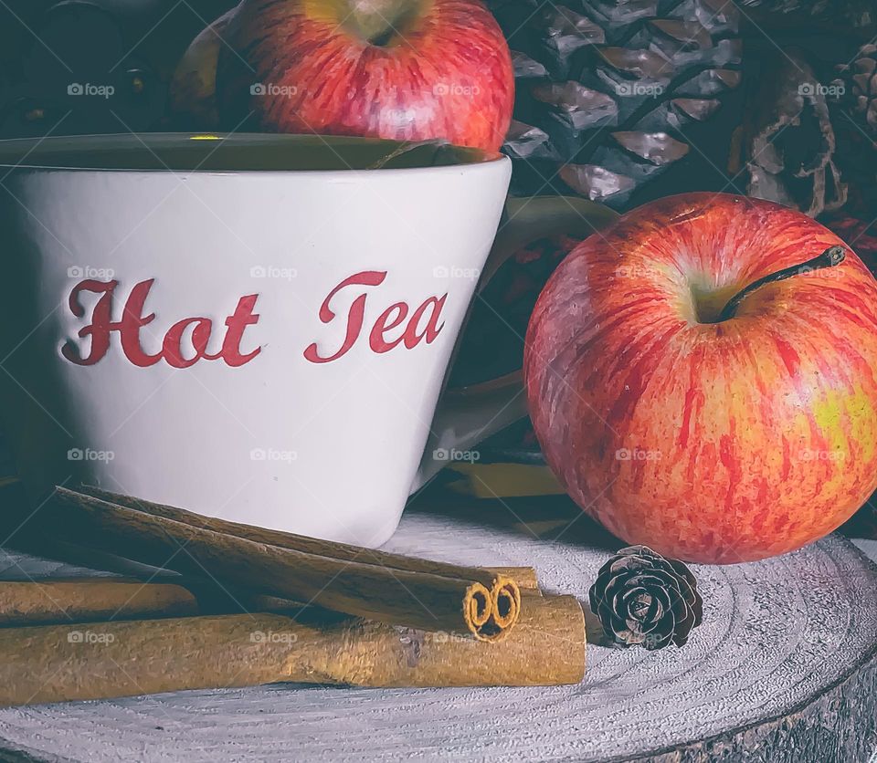 Hot apple & cinnamon tea on wood platter, with fruit, spices and pine cones