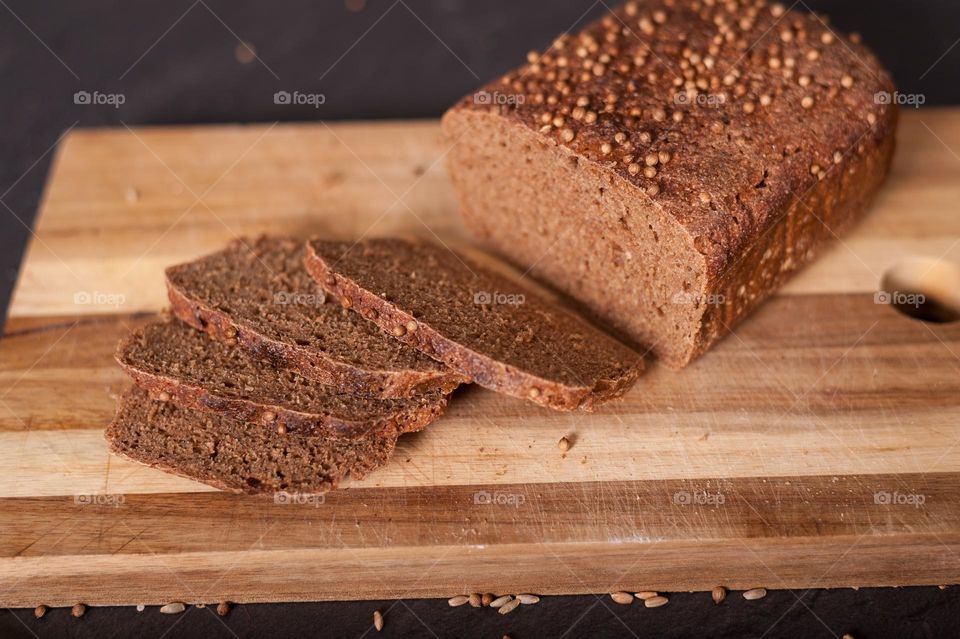 Freshly home baked, wholegrain, rye, sliced brown loaf of bread wooden kitchen board.