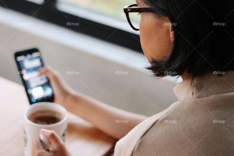 A girl having a cup of coffee while she looking at her media social through smart phone