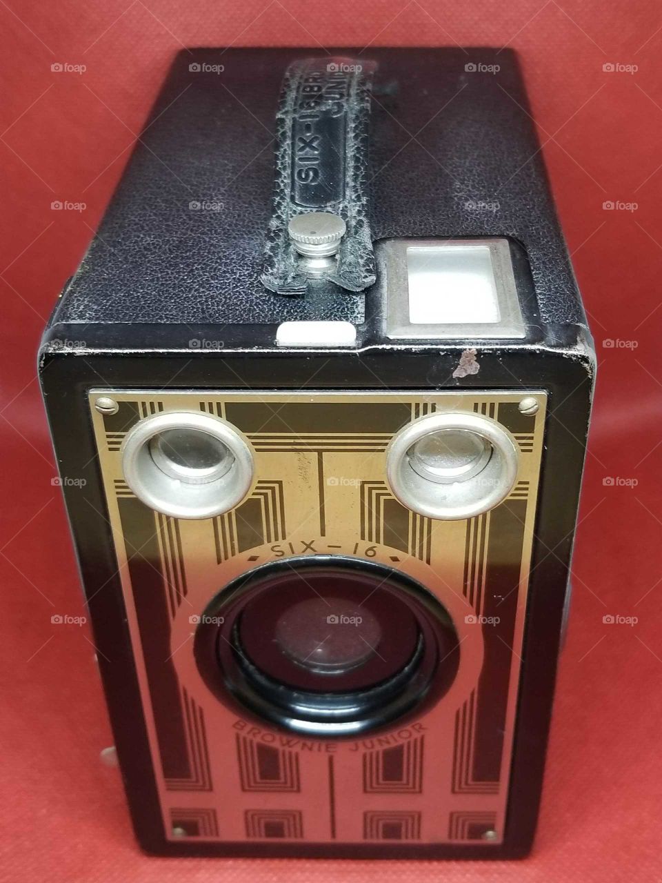 Kodak Brownie 616 from 1930's box style portrait camera with gold and black front.  Has art deco look. On red background.