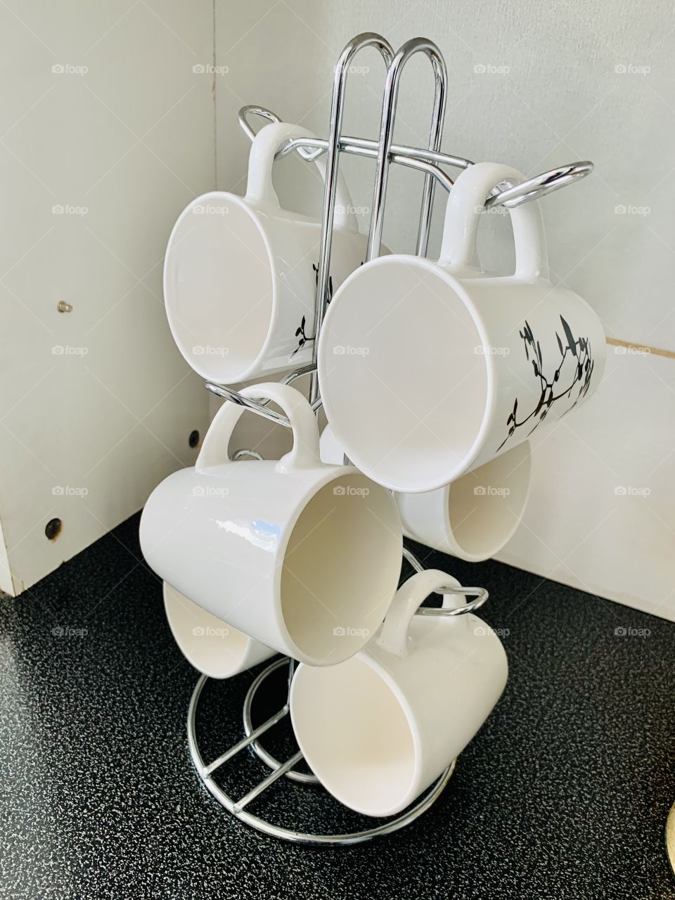 White coffee mugs hanging on a metal cup holder in a corn of a cupboard in the kitchen.