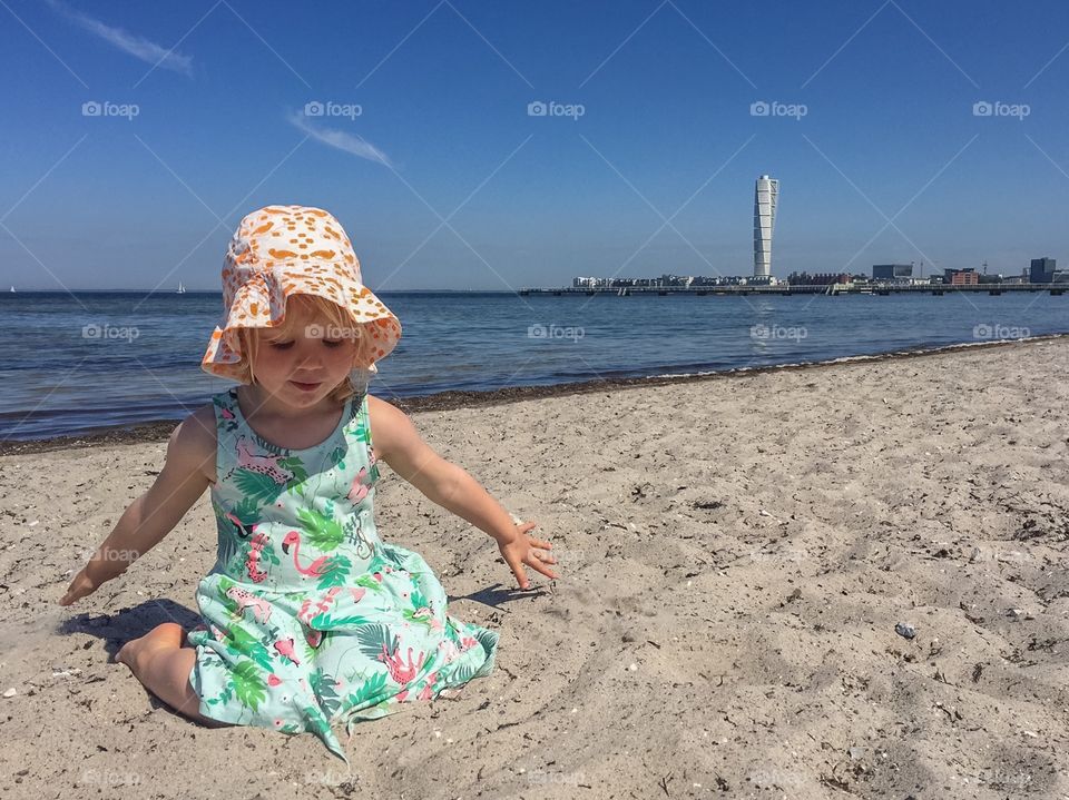 Little girl of three years old playing in the sand at Ribban bech in Malmö Sweden with the famous skyscraper Turni g Torso in the background.